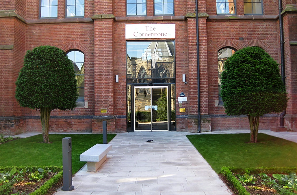 Rechts und links neben dem Eingang eines Backsteingebäudes steht je ein Baum die Krone als Bienenkorb geschnitten