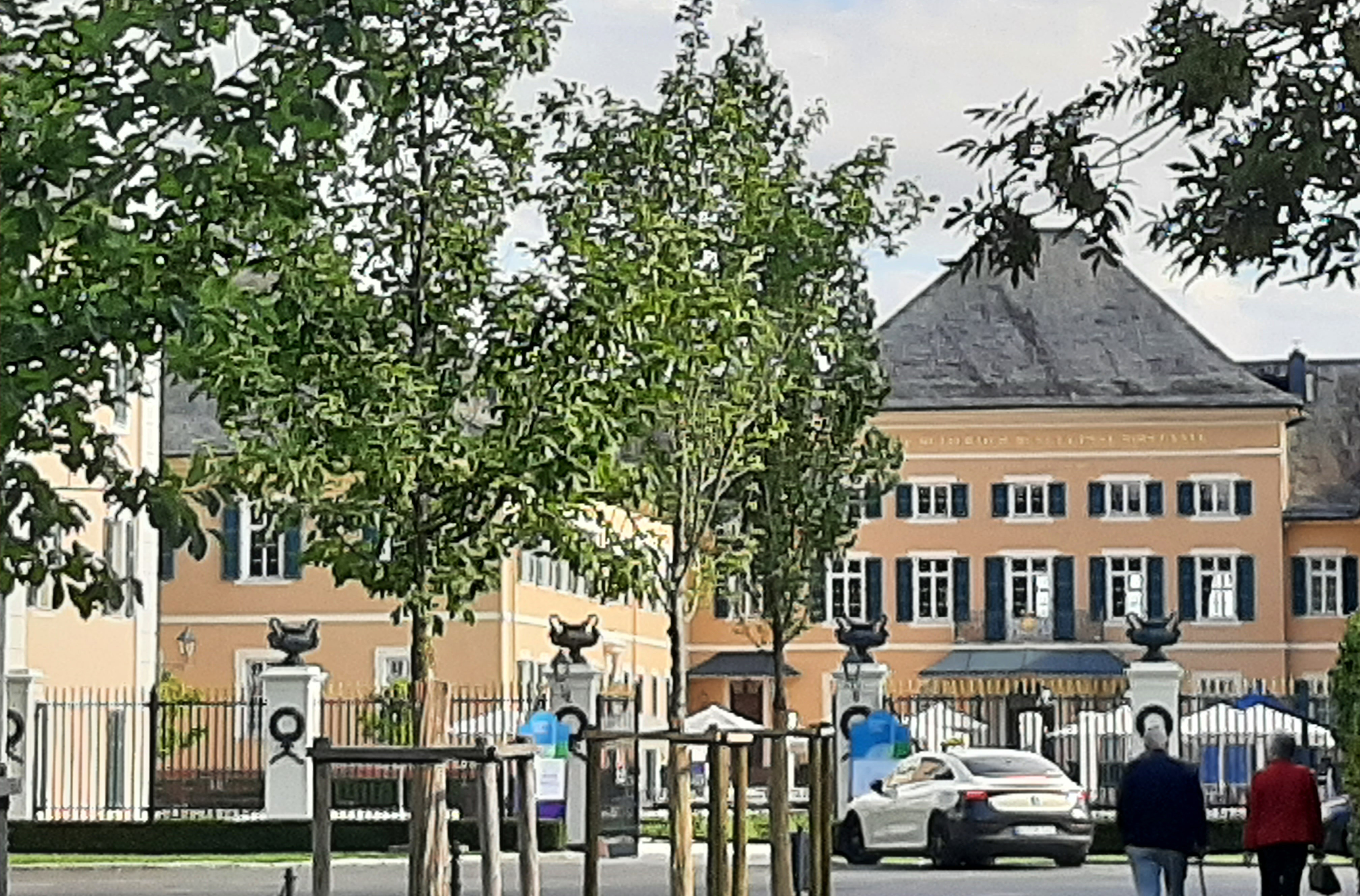 vor dem sandfarbenen Schloss stehen frisch gepflanzte Bäume